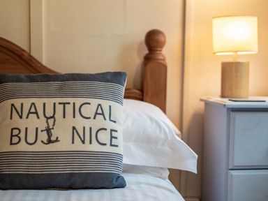 A bed with a pillow that reads nautical but nice a wooden bedpost and a nightstand with a lamp at St Samson in Port Isaac