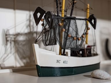 A model fishing boat with nets and floats on a surface with a seashell nearby at St Samson in Port Isaac