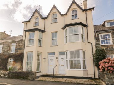 The exterior of a beige semi detached house with two white front doors and three peaked roof sections at Bay View in Criccieth