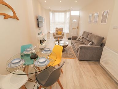 A living room with a glass dining table and multicolored chairs a gray sofa a patterned armchair and a coffee table at Bay View in Criccieth