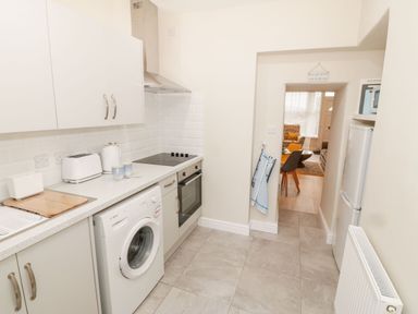 A kitchen with white cabinets a washing machine an oven a fridge and a view into a dining area at Bay View in Criccieth