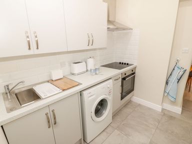 A kitchen with white cabinets a washing machine an oven a stove two mugs a toaster and a sink at Bay View in Criccieth