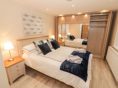 A bedroom with a bed with pillows and blankets two bedside tables with lamps and a wardrobe with mirrored sliding doors at Bay View in Criccieth
