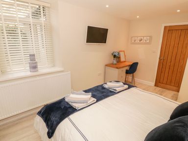 A bedroom with a bed and folded towels on it a desk with a blue chair and flowers a wall-mounted TV and a wooden door at Bay View in Criccieth