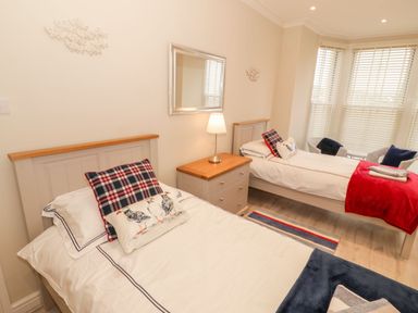 A bedroom with two single beds a nightstand with a lamp a mirror on the wall and two chairs by a window at Bay View in Criccieth