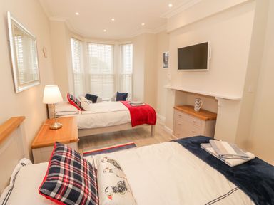 A bedroom with two single beds a wall-mounted TV and bay windows at Bay View in Criccieth