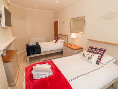A bedroom with two single beds a television on the wall and a dresser with a lamp at Bay View in Criccieth