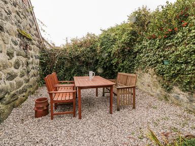 An outdoor patio area with wooden table and benches surrounded by stone walls with ivy at Bay View in Criccieth