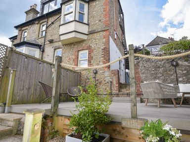 An outdoor patio with chairs and a rope railing beside a stone house at Coastal View in Lyme Regis