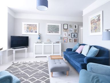 A living room with blue sofas grey ottoman and a television at Coastal View in Lyme Regis