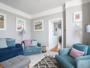 A living room with blue and teal sofas pink and blue cushions floor lamp framed pictures on walls and a patterned rug