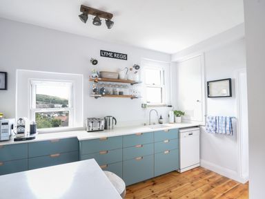 A kitchen with blue cabinets white countertops wooden floor and windows overlooking outside at Coastal View in Lyme Regis