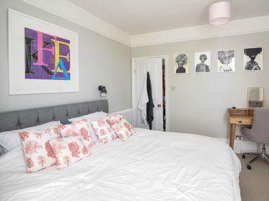 A bedroom with a large bed and decorative pillows a wall with framed artwork a wooden desk with a chair and a mirror Coastal View Lyme Regis