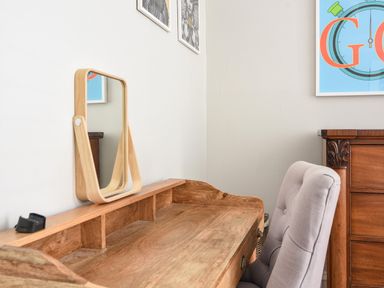A wooden desk with a small mirror on it and a gray cushioned chair next to a wooden dresser in a room at Coastal View in Lyme Regis