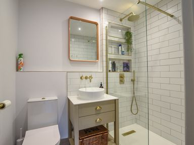 A bathroom with a toilet a sink with two drawers a mirror and a glass enclosed shower with built in shelves at Coastal View in Lyme Regis