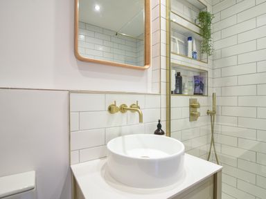 A bathroom with a round white sink a wall-mounted brass faucet built-in shelves with toiletries and a mirror at Coastal View in Lyme Regis