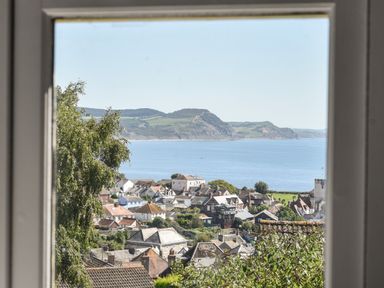 View of a coastal town with houses trees and a sea with hills in the background from a window at Coastal View in Lyme Regis