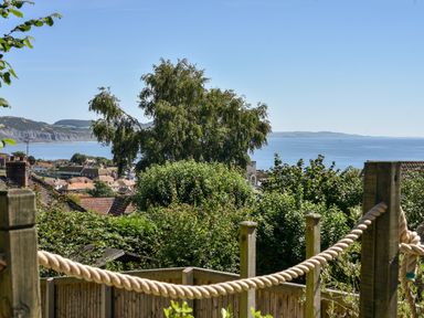 A garden with wooden posts and rope fencing overlooking trees rooftops and the sea at Coastal View in Lyme Regis