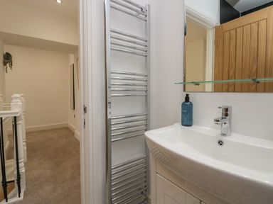 A bathroom sink with a faucet and soap dispenser beside a towel rack and an open door leading to a carpeted hallway at Dalegarth Hall Farm Cottage 1 Boot near Eskdale Green