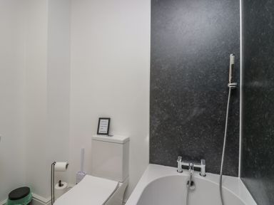 A bathroom with a toilet, toilet paper holder, toilet brush, small bin, and a bathtub with a handheld shower at Dalegarth Hall Farm Cottage 1 Boot near Eskdale Green