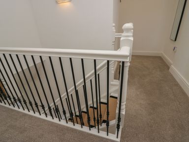 A stairway with a white banister and black spindles in a carpeted hallway at Dalegarth Hall Farm Cottage 1 Boot near Eskdale Green