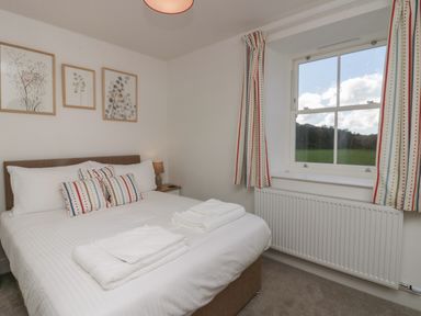 A bedroom with a bed with striped pillows and folded towels on it a bedside table with a lamp three framed pictures on the wall and a window with striped curtains at Dalegarth Hall Farm Cottage 1 Boot near Eskdale Green