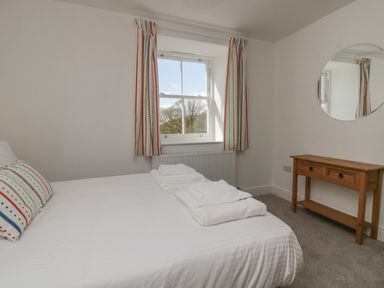 A bedroom with a bed white linens two pillows folded towels a window with curtains and a wooden table with a round mirror at Dalegarth Hall Farm Cottage 1 in Boot near Eskdale Green