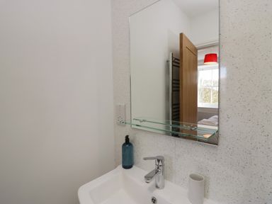 A bathroom sink with a blue soap dispenser beside it and a mirror above showing a wooden door and window with a red lamp shade at Dalegarth Hall Farm Cottage 1 Boot near Eskdale Green