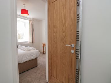 A view into a bedroom through a wooden door with a bed a bedside table and a window with curtains at Dalegarth Hall Farm Cottage 1 Boot near Eskdale Green
