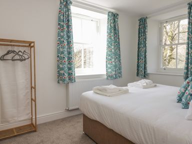 A bedroom with a double bed with white linens and towels with patterned curtains and a wooden clothes rack at Dalegarth Hall Farm Cottage 1 Boot near Eskdale Green