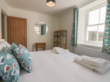A bedroom with a bed and patterned cushions a wooden door a round mirror a window with curtains and a wooden shelving unit at Dalegarth Hall Farm Cottage 1 Boot near Eskdale Green