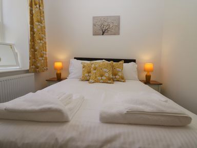 A bedroom with a bed with white linens yellow patterned pillows two bedside tables with lamps and a painting above the bed at Dalegarth Hall Farm Cottage 1 Boot near Eskdale Green