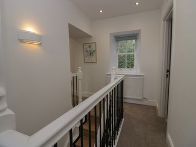 A hallway with a staircase railing a window a framed picture and a wall light at Dalegarth Hall Farm Cottage 1 Boot near Eskdale Green