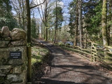 A dirt road with trees on both sides and a stone wall with a Dalegarth Hall Farm Cottages sign at Boot near Eskdale Green