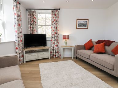 A living room with two sofas a television on a stand a side table with a lamp and patterned curtains at Dalegarth Hall Farm Cottage 1 Boot near Eskdale Green