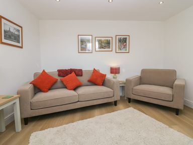 A living room with a beige sofa and armchair with orange cushions a small table with a lamp and framed pictures on walls at Dalegarth Hall Farm Cottage 1 Boot near Eskdale Green