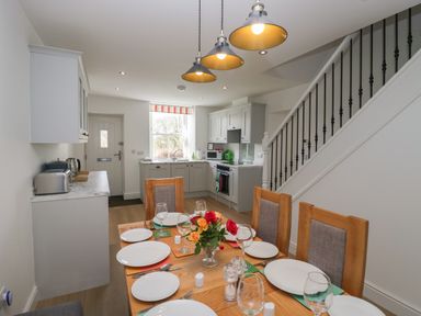 A kitchen and dining area with a wooden table set with plates and glasses next to a staircase at Dalegarth Hall Farm Cottage 1 Boot near Eskdale Green