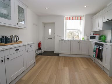 A kitchen with white cabinets wooden floor a window a door a microwave an oven and kitchen accessories at Dalegarth Hall Farm Cottage 1 Boot near Eskdale Green