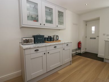 A kitchen area with white cabinets a toaster bread bin kettle and glassware at Dalegarth Hall Farm Cottage 1 Boot near Eskdale Green