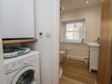 A washing machine and dryer in a laundry area next to a bathroom with a toilet sink and window at Dalegarth Hall Farm Cottage 1 Boot near Eskdale Green