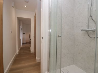 A hallway with wooden flooring and white walls next to a shower with glass doors and marble patterned walls at Dalegarth Hall Farm Cottage 1 Boot near Eskdale Green