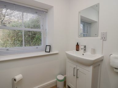 A bathroom with a window with blinds a sink cabinet a mirror a soap dispenser a toilet paper holder and a trash bin at Dalegarth Hall Farm Cottage 1 Boot near Eskdale Green