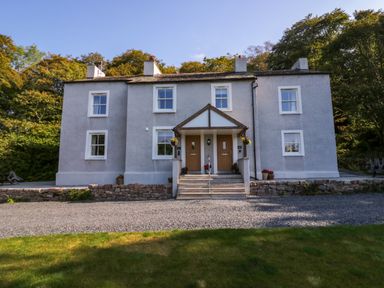 A two-story gray house with two front doors and a small porch area surrounded by trees at Dalegarth Hall Farm Cottage 1 Boot near Eskdale Green