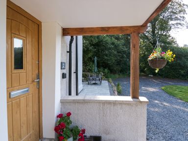 A wooden front door with flowers in a pot and a hanging flower basket on a porch at Dalegarth Hall Farm Cottage 1 Boot near Eskdale Green