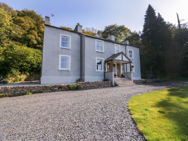 A two story house with a gravel driveway and green lawn surrounded by trees at Dalegarth Hall Farm Cottage 1 Boot near Eskdale Green