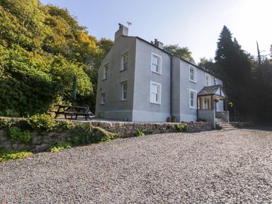 A grey two-story house with white window frames and a stone driveway surrounded by trees at Dalegarth Hall Farm Cottage 1 Boot near Eskdale Green