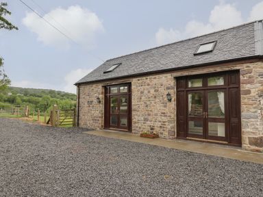 An exterior view of a stone building with two wooden framed glass doors and a gravel yard at Gelli Barn Near Llandeilo