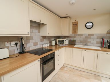 A kitchen with wooden countertops cream cabinets an electric stove oven a toaster a kettle a microwave and a sink with a clock on the wall at Gelli Barn Near Llandeilo