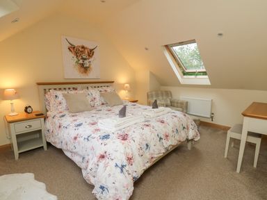 A bedroom with a double bed floral bedding armchair and a desk under a skylight window at Gelli Barn Near Llandeilo