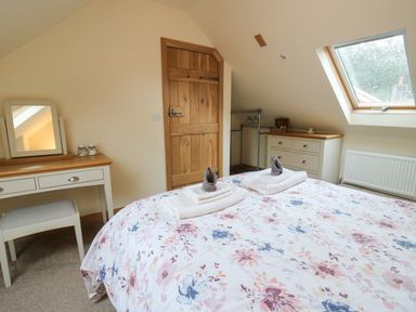 A bedroom with a floral bedspread two towels on the bed a wooden door a dressing table a chest of drawers and a skylight window at Gelli Barn Near Llandeilo